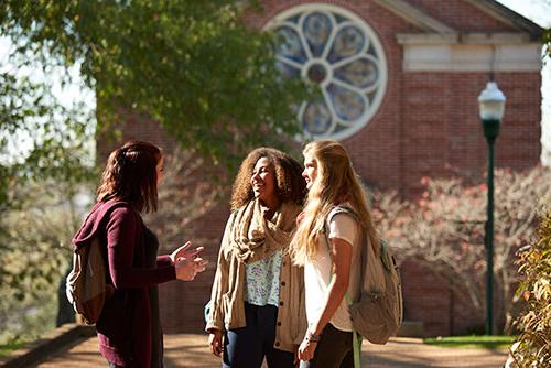 Three female student stand in front of the chapel talking