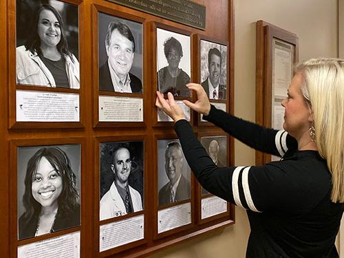 Leslie Sebaugh adjusts a photo on the Wall of Distinguished Alumni