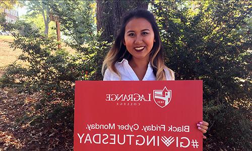 Student poses with college sign that reads "Black Friday. Cyber Monday. #GivingTuesday